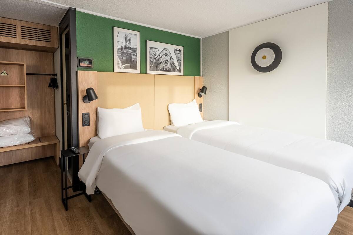 Ein Hotelzimmer mit zwei Betten, einem Holzschrank, einer grünen Akzentwand und zwei gerahmten Bildern.