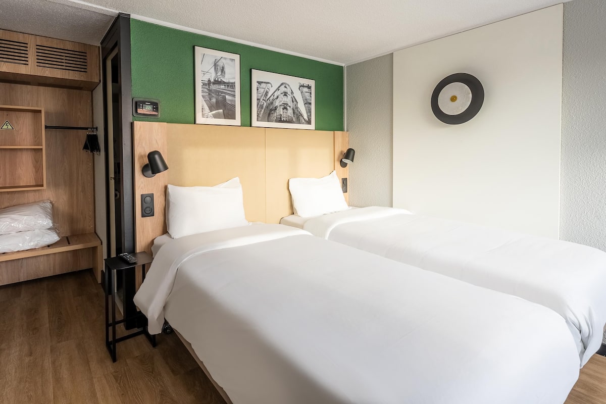 Una habitación de hotel con dos camas, un armario de madera, una pared de acento verde y dos cuadros enmarcados.