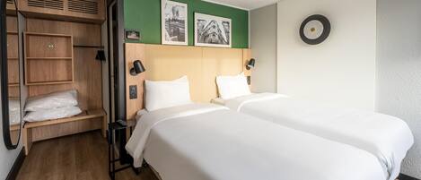 Una habitación de hotel con dos camas, un armario de madera, una pared de acento verde y dos cuadros enmarcados.