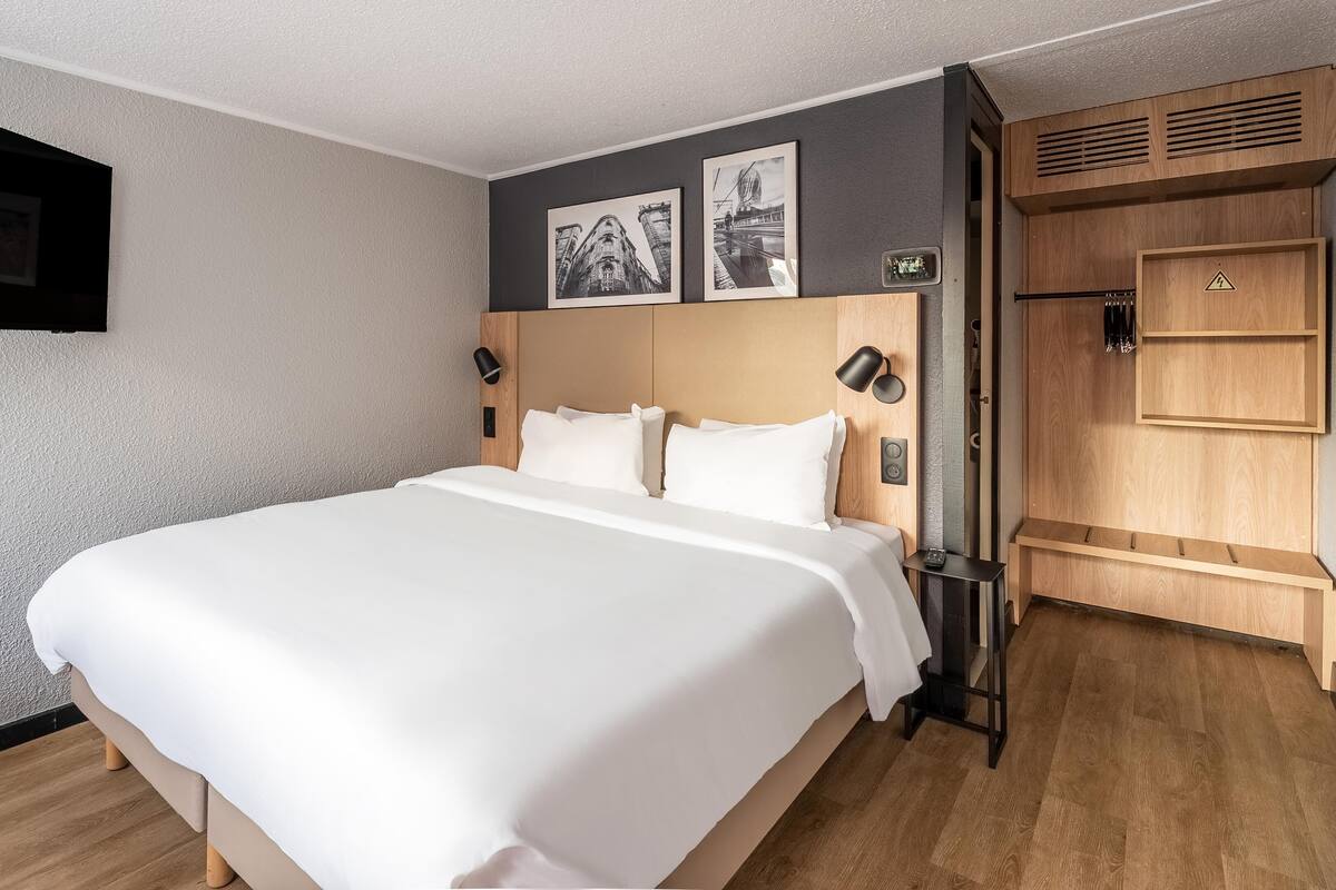 Ein Hotelzimmer mit einem großen Bett, einem flachbildfernseher an der Wand und einem Holzschrank.
