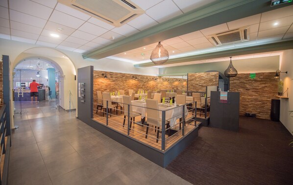 A modern restaurant with a central island, multiple tables, and a stone wall backdrop.