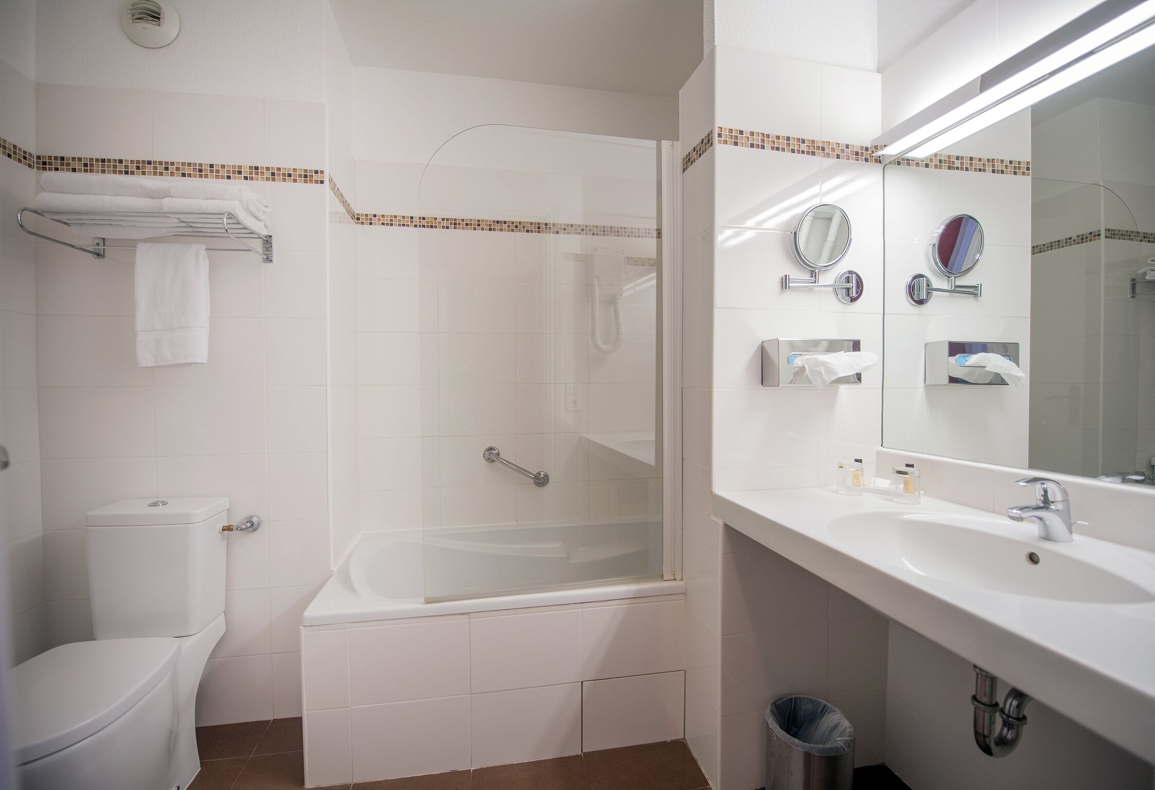 A bathroom with a toilet, bathtub, and a sink with mirrors.