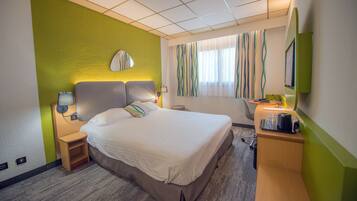 Habitación de hotel con cama, mesitas de noche, escritorio con silla, espejo y ventana con cortinas.