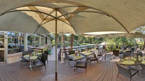 An outdoor dining area with tables and chairs under large umbrellas, overlooking a pool and greenery. - Promotel Carros (Carros)