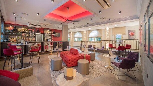 A modern bar area with a red ceiling, multiple seating options including red and purple chairs, and a bar stocked with various bottles. - Promotel Carros (Carros)