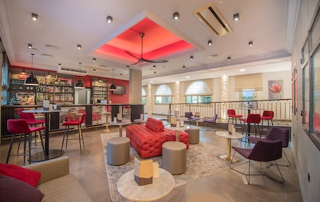 A modern bar area with a red ceiling, multiple seating options including red and purple chairs, and a bar stocked with various bottles.