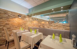 A restaurant with wooden wall decor, tables with white tablecloths, and green napkins.