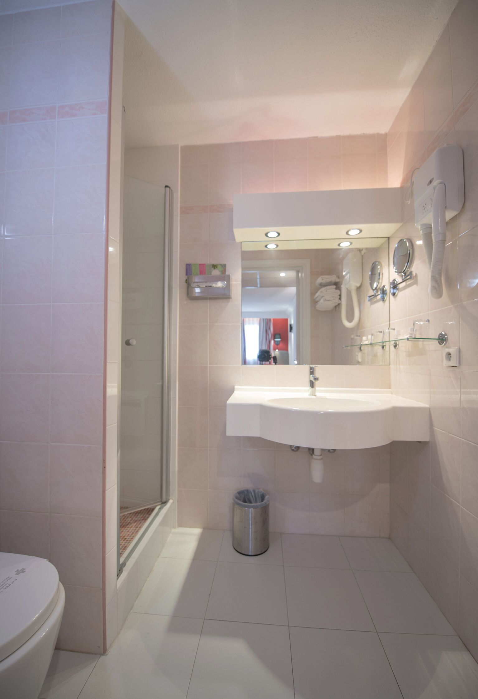 Un baño con cabina de ducha de vidrio, un lavamanos blanco y un espejo sobre él.