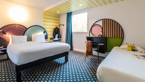 A hotel room with two beds, a desk, a chair, a window with curtains, and a patterned floor.