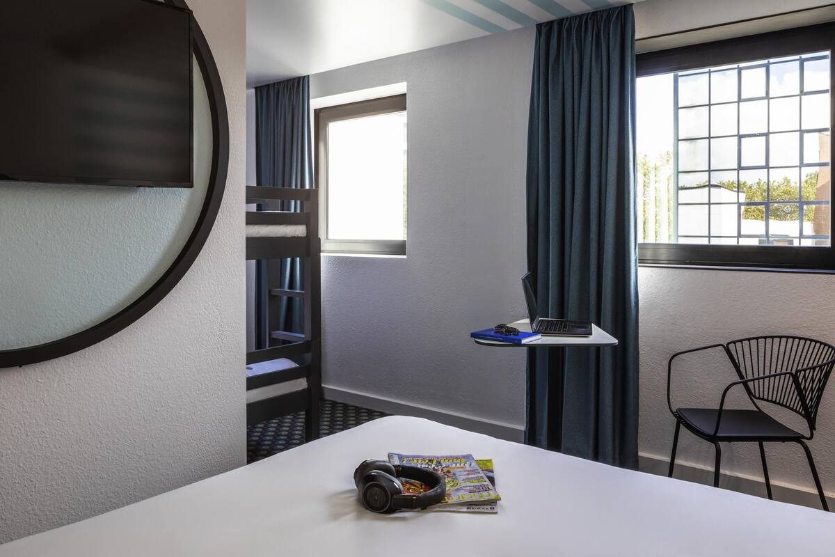 Una habitación con literas, un escritorio con una computadora portátil, una silla y un ventanal con cortinas.