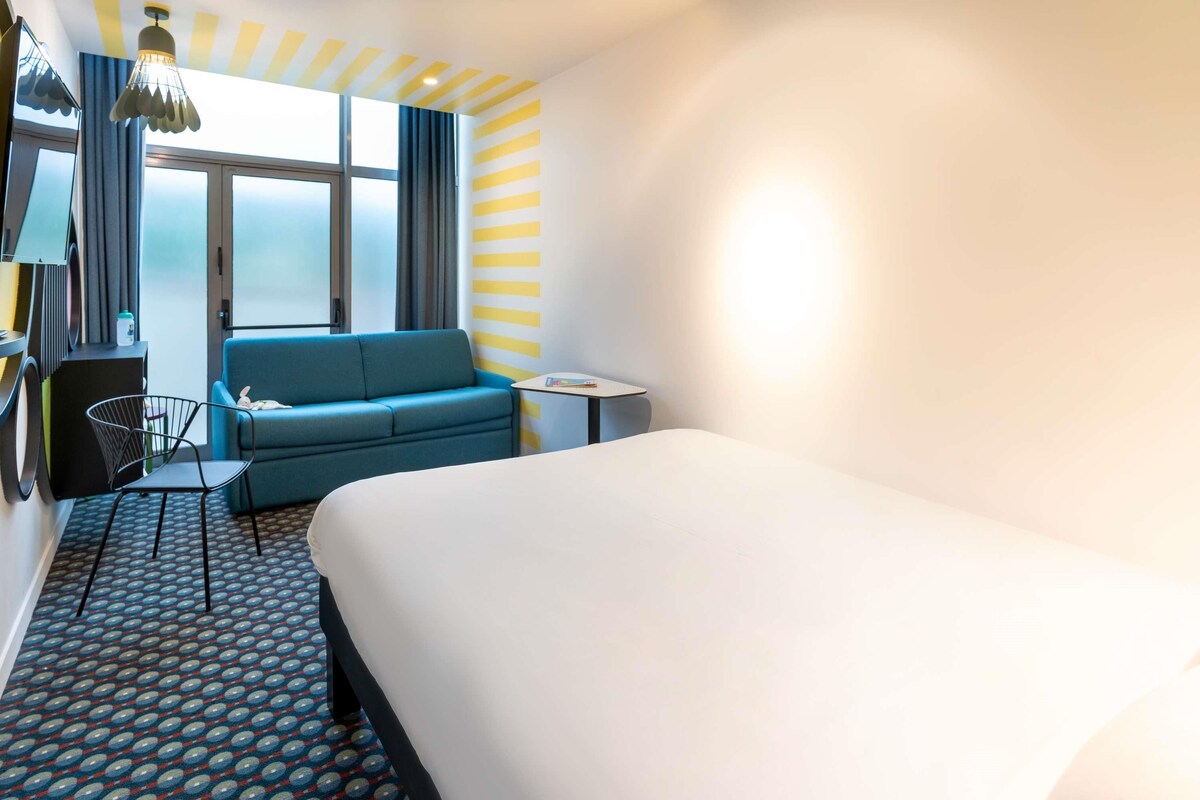 Una habitación de hotel con una cama grande, un sofá azul, una mesita y una alfombra estampada.