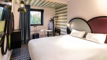 A hotel room with a bed, a small table, a chair, a suitcase, and a window with curtains.