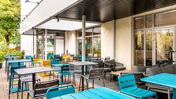 Un café en plein air doté de nombreuses tables et chaises, de grandes fenêtres et d’un espace salon abrité.