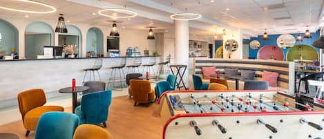 A modern bar area with a foosball table, comfortable seating, and a bar counter.