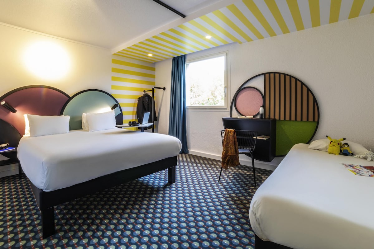 Habitación de hotel con dos camas, un escritorio, una silla, un espejo y una ventana con cortinas.
