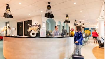 Zona de recepción de hotel con mostrador curvo, una recepcionista y un huésped de pie.