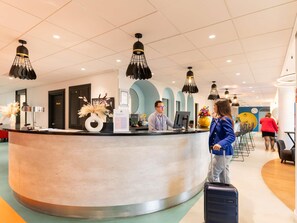 Un espace d’accueil d’hôtel avec un comptoir incurvé, un réceptionniste et un client debout.