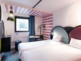 Camera d'albergo con un letto, una scrivania, una sedia, un lampadario, una finestra con tende e un termosifone.