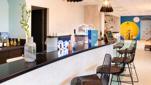 Een bar met een toonbank, krukken en een koffieapparaat.