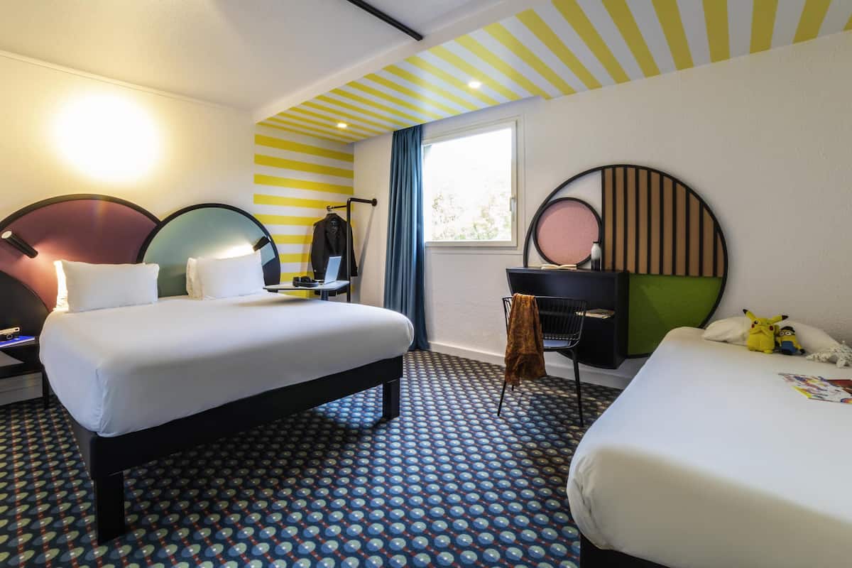 Habitación de hotel con dos camas, un escritorio, una silla, un espejo y una ventana con cortinas.
