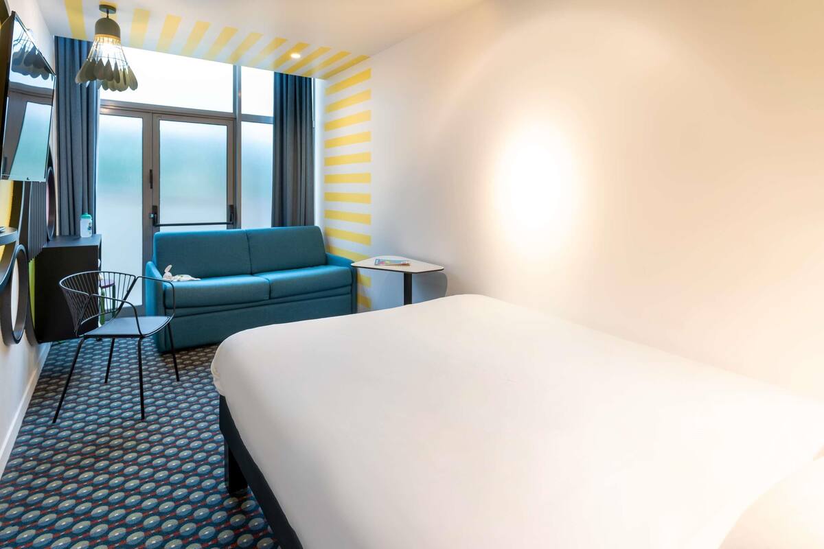 Una habitación de hotel con una cama grande, un sofá azul, una mesita y una alfombra estampada.