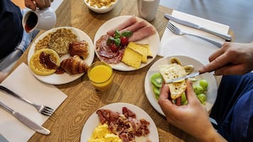 En frukostuppläggning med tallrikar fyllda med ägg, bacon, croissanter och rostat bröd, samt en kopp kaffe och ett glas apelsinjuice.