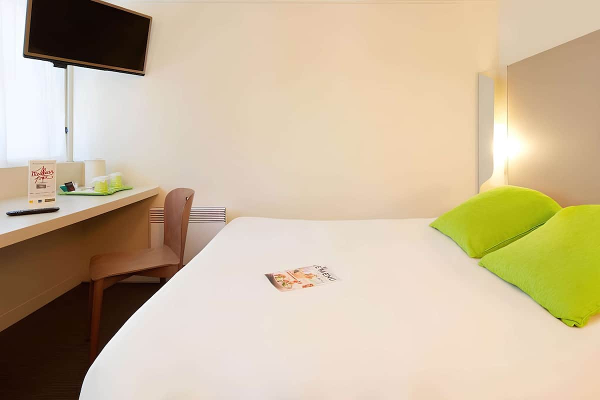 Habitación de hotel con cama, escritorio, silla, televisión y mesita de noche con control remoto y tarjeta de menú.