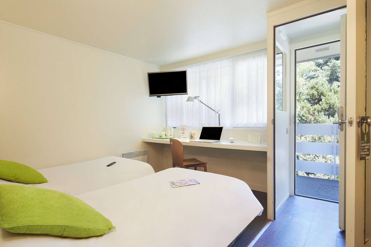Habitación de hotel con dos camas, un escritorio con una computadora portátil, un televisor y vista al exterior.