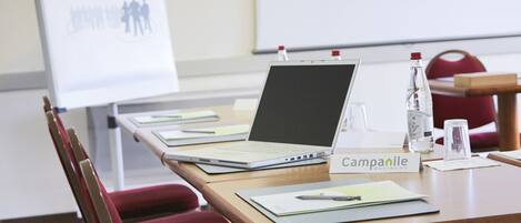 Un salón de conferencias con una computadora portátil sobre una mesa, una botella de agua, un vaso y una placa con el nombre 'Campanile Business'.