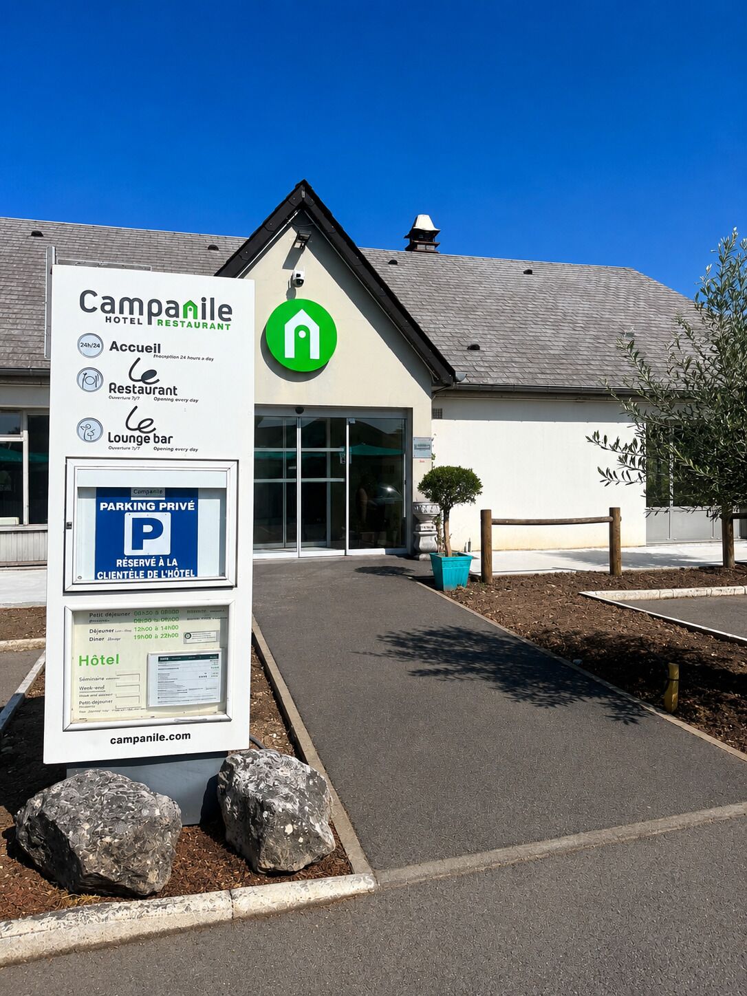 A hotel entrance with a sign indicating 24-hour access, a restaurant, and a lounge bar.