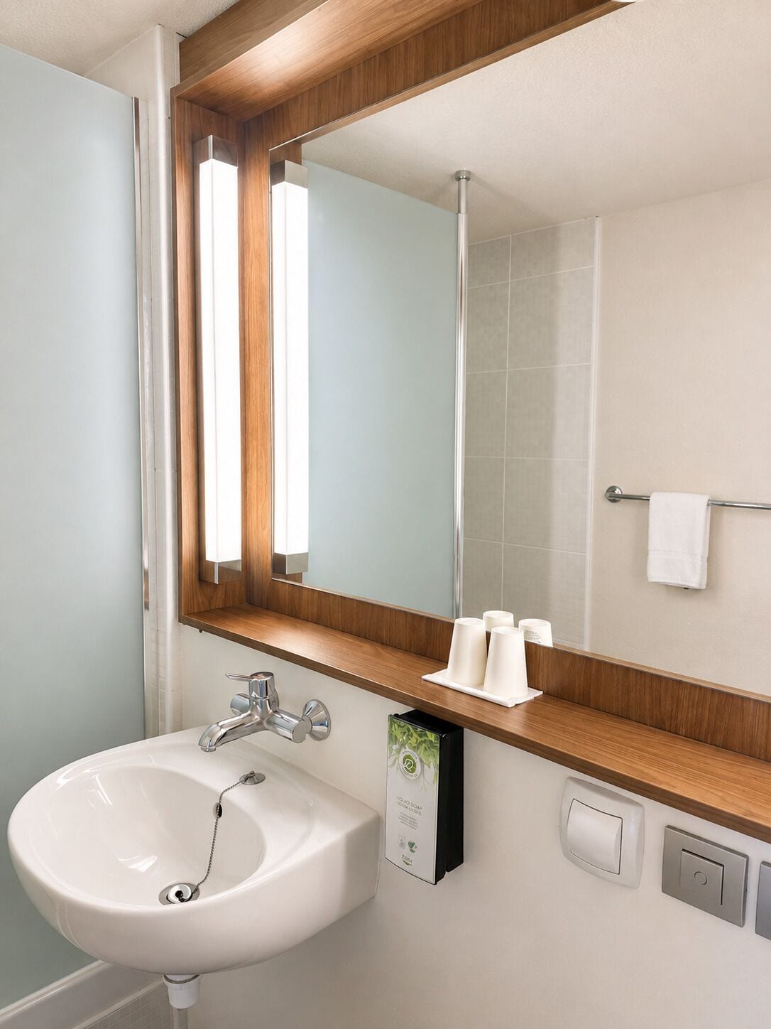 Un baño con lavamanos blanco, espejo con marco de madera y un perchero para toallas.
