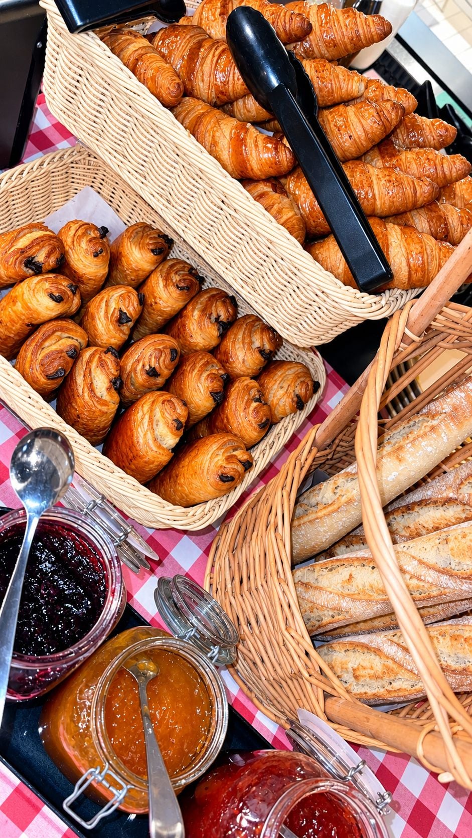 Een tafel met manden vol gebak en brood, en potten vol jam.