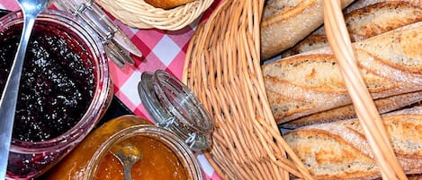 Une table avec des paniers remplis de viennoiseries et de pain, ainsi que des pots de confiture.
