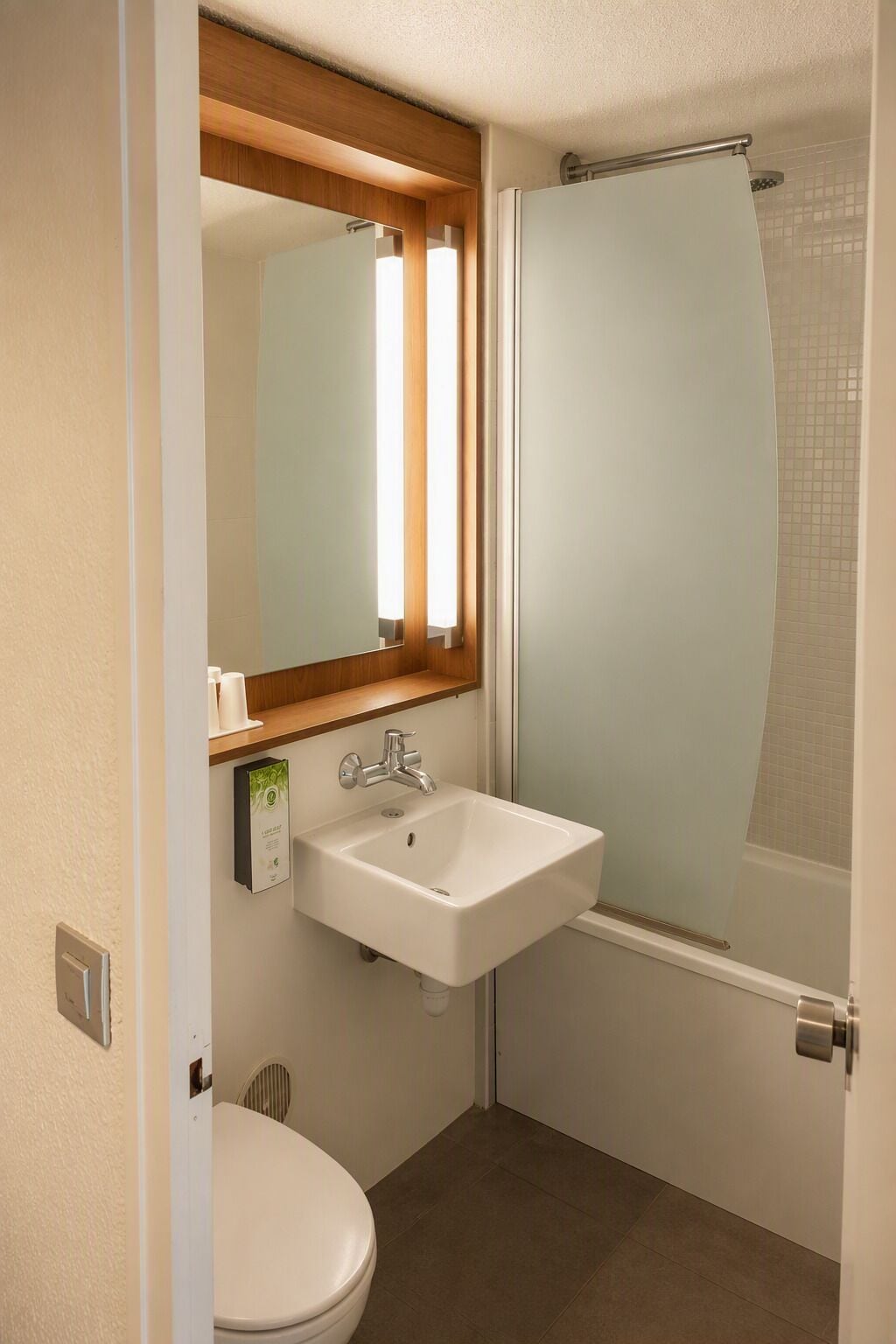 Een badkamer met een wit wastafel, toilet en douche met een matglazen deur.