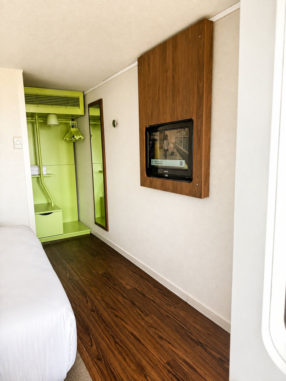 Una habitación con una cama, un televisor en la pared y un espejo.