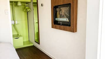 Una habitación con una cama, un televisor en la pared y un espejo.