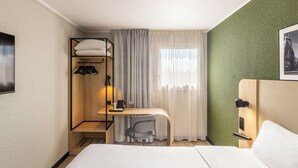 Habitación de hotel con cama, escritorio y silla, perchero y ventana con cortinas.