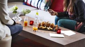 A modern living room with a wooden coffee table, a vase with flowers, a bottle of water, a glass of orange juice, and a plate of pastries. - Campanile PRIME - Paris Bobigny (Bobigny)