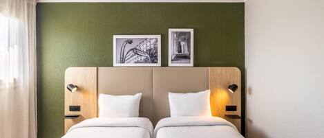 Une chambre d’hôtel avec deux lits, un mur vert à texture et deux tableaux encadrés au-dessus des lits.