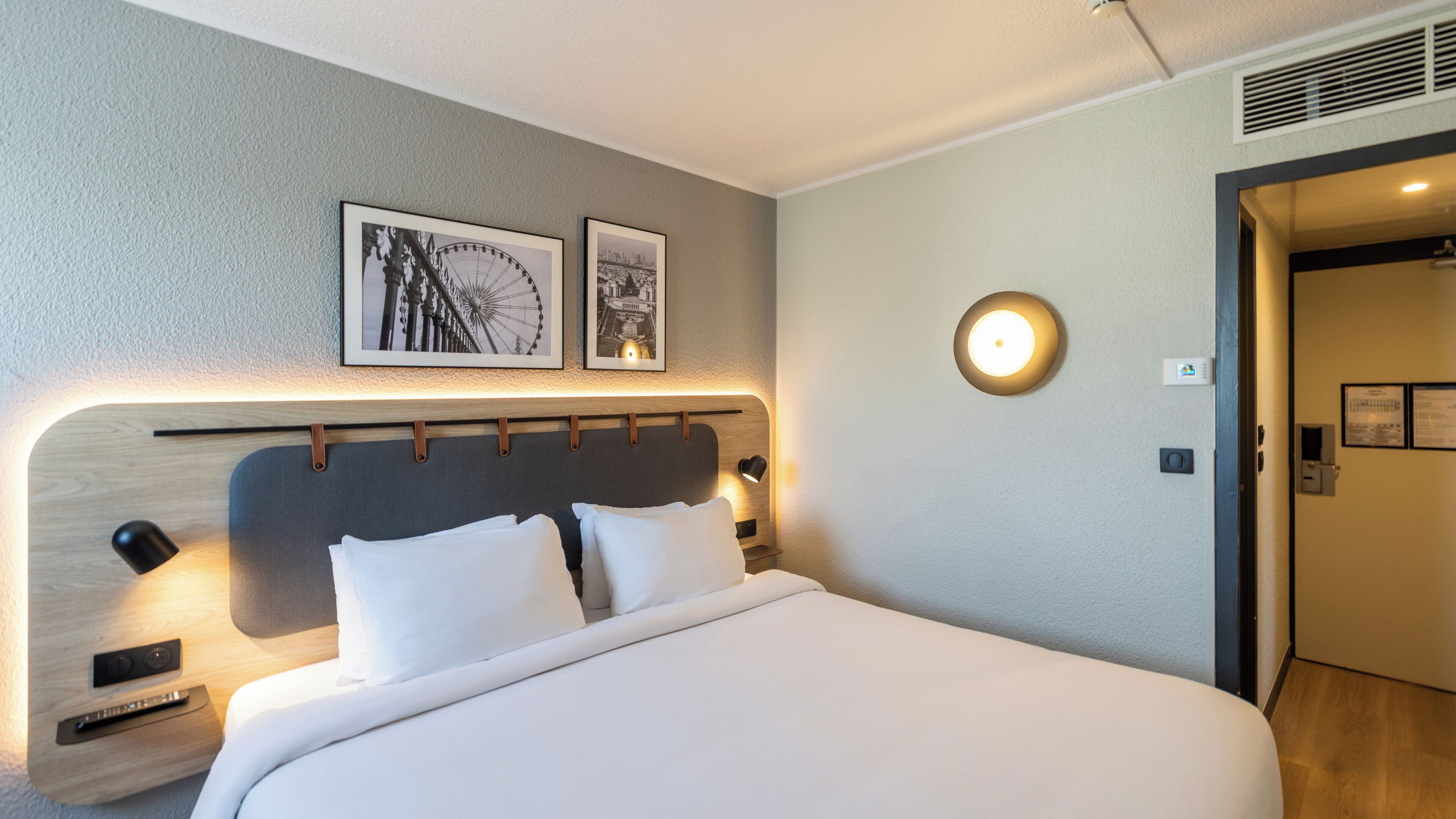 Habitación de hotel con cama, lámparas de noche, cabecera y dos cuadros en la pared.