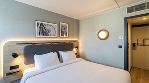 Habitación de hotel con cama, lámparas de noche, cabecera y dos cuadros en la pared.