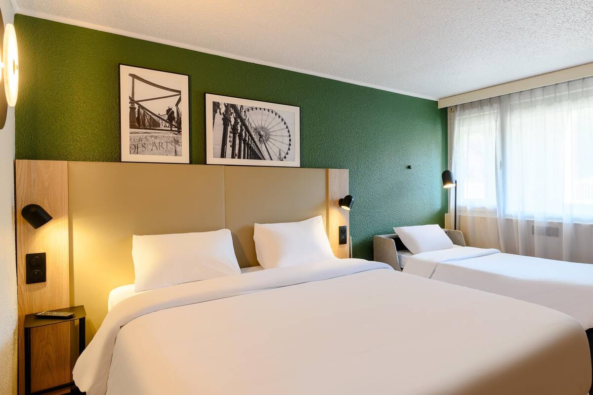 A hotel room with two beds, a green textured wall, and two framed pictures.