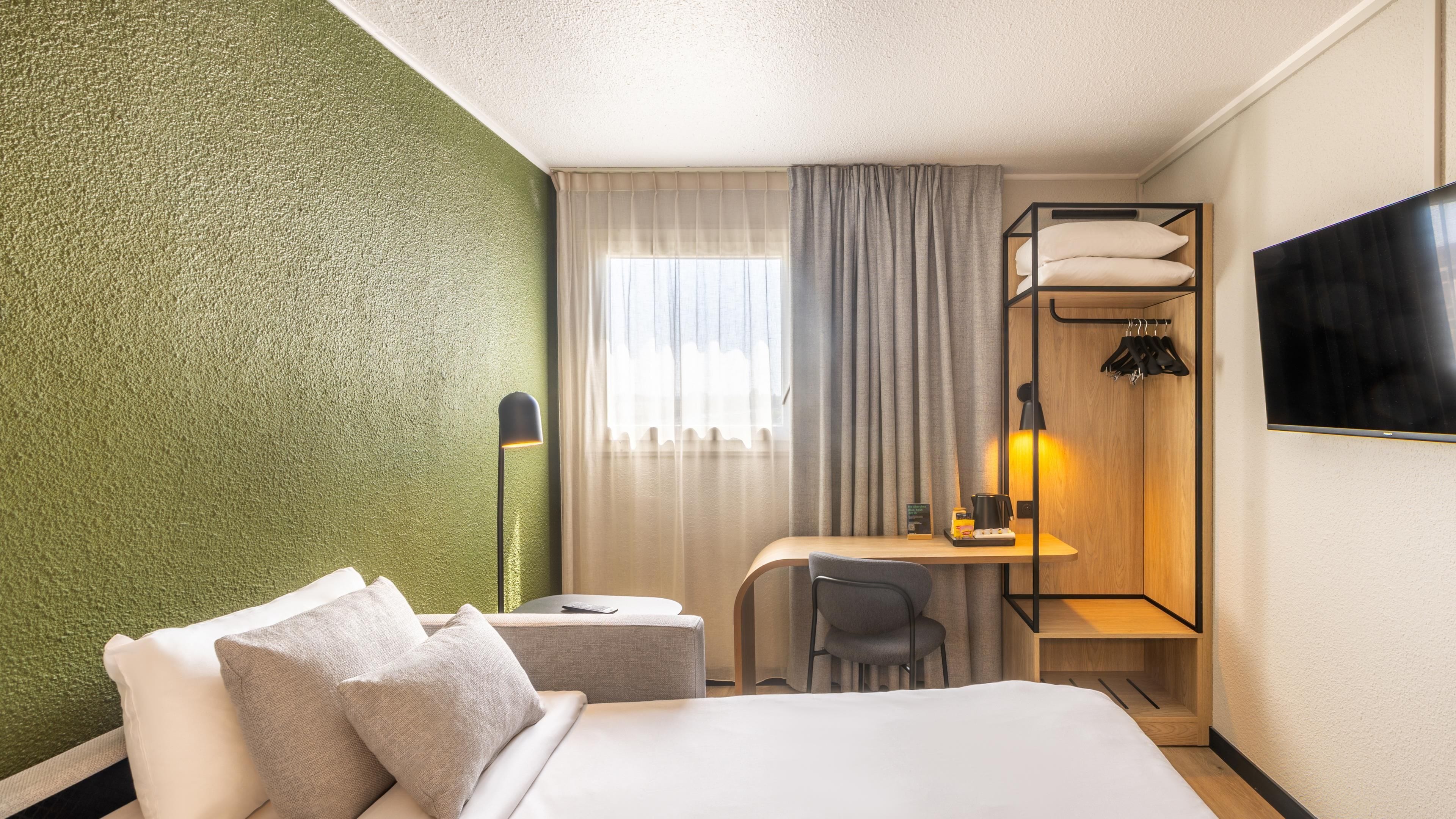 Een hotelkamer met een bed, een bureau, een stoel, een lamp en een televisietoestel.