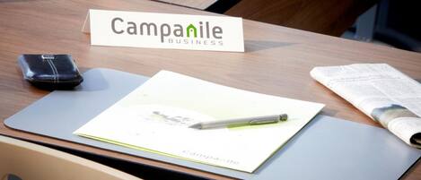 A wooden table with a 'Campanile Business' sign, a wallet, a notepad, a pen, and a newspaper.