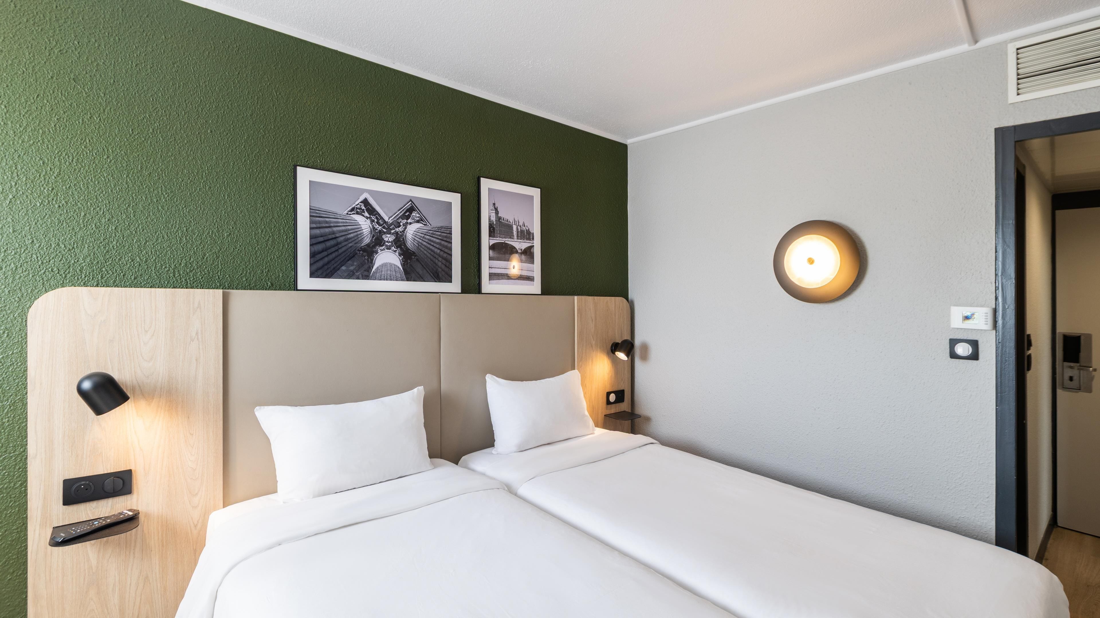 Ein Hotelzimmer mit einem Bett, zwei Kissen, einem Kopfteil, einer Wandleuchte und zwei gerahmten Bildern.