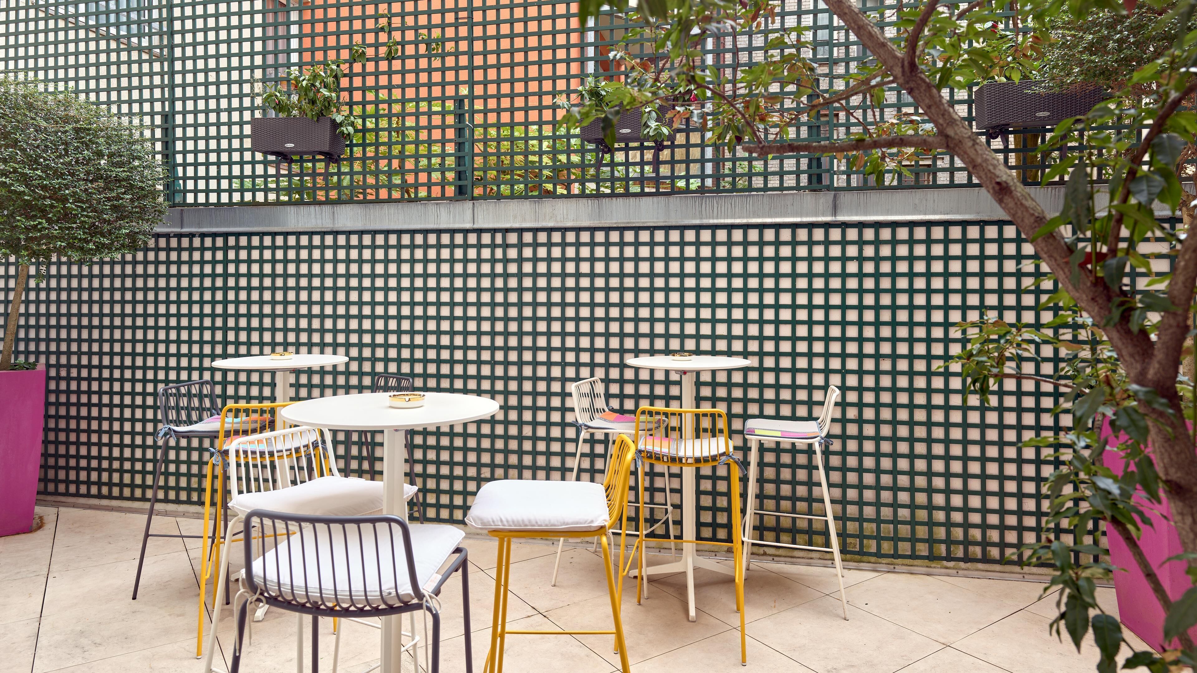 An outdoor seating area with tables and chairs, a green lattice fence, and a potted plant.