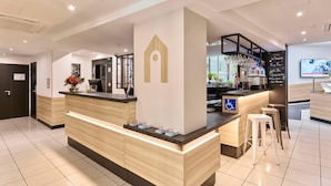 Zona de recepción de hotel con mostrador, señal de acceso para discapacitados, área de bar con vasos y una pantalla de televisión.