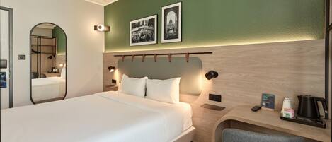 Habitación de hotel con cama, escritorio, silla, espejo y dos cuadros en la pared.