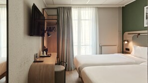 A hotel room with a bed, bedside table, lamp, and a view of the outside.