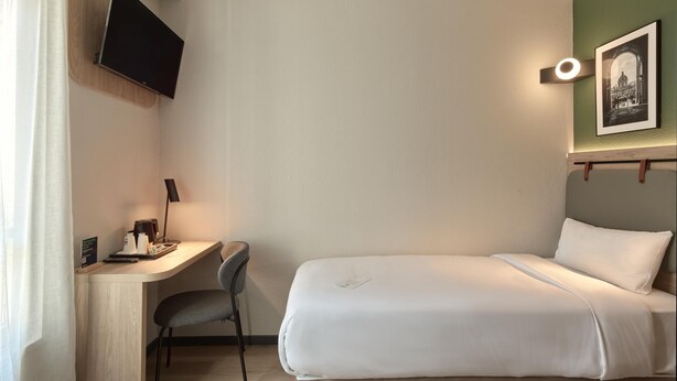 A hotel room with a bed, desk, chair, TV, and a framed picture on the wall.